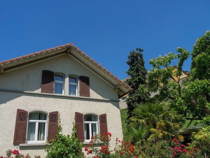 Residential house with brown shutters and a lushly planted garden in bright sunshine, Meersburg,