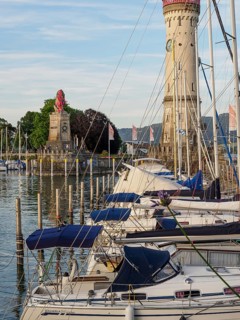Boats in the harbour with lighthouse and lion sculpture in the background on a sunny day,