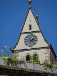 Close-up of a church tower with clockwork and spire against a clear blue sky in the sunshine,