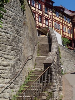 Stone staircase leads between old half-timbered houses and a stone wall in the sun, Meersburg,