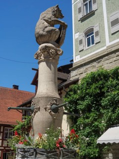 Large bear statue on a fountain in front of a historic building, surrounded by flowers on a sunny