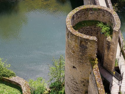 A round, old stone tower located by a quiet river and surrounded by a stone wall, Luxembourg City,