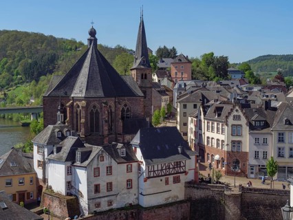 View of a historic town with churches and half-timbered houses next to a river in sunny weather,