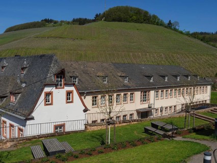 Large building in the middle of a rural, hilly landscape with meadows and trees in sunny weather,