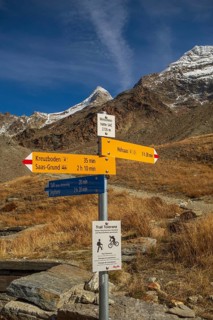 A signpost on a hiking trail in the mountains under a clear blue sky, surrounded by dry landscape