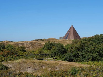 Landscape with pyramid structure in the background, surrounded by dunes and bushes on a sunny day,