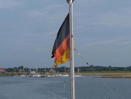 A German flag on a boat, surrounded by water and a quiet harbour, Spiekeroog, East Frisia, GERMANY
