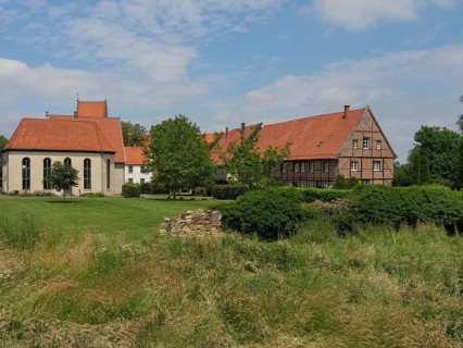 View of an estate with a church, tiled roofs, surrounded by lawns and trees under a blue sky,