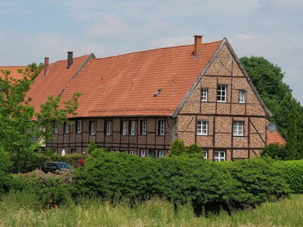 Large half-timbered house with red tiled roof surrounded by green bushes and trees on a summer's