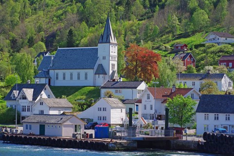 Village with church on a green hill, surrounded by wooden houses and a ferry pier, Utne, Hardanger,