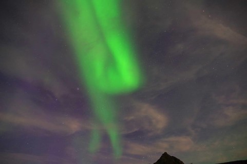 Green Northern Lights stretching across a mountain landscape against a starry night sky, Nyksund,