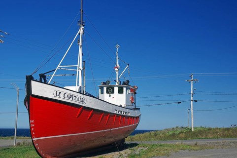 Red boat on land next to a coastal road under a clear blue sky, Gaspesie, St. Lawrence River,