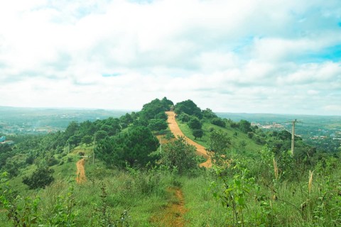 A serene hill with a winding path surrounded by lush greenery under a partly cloudy sky in the