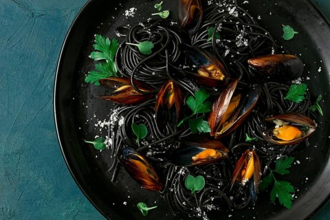 Spaghetti with black squid, black pasta, with boiled mussels, on a black plate, with parsley and