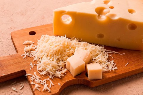 Geriebener Käse, Maasdam, auf einem Schneidebrett, Reibe und Käsemesser, Nahaufnahme, keine