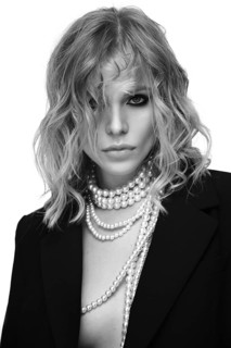 A beautiful woman with loose hair, in a jacket and beads, poses in the studio on a white background