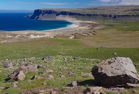 A vast coastal panorama with green hills and rugged cliffs, bordering a deep blue sea, Latrabjarg,