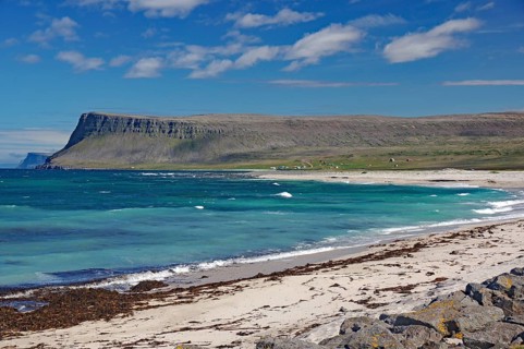 A clear day on a sandy beach with waves crashing against the shore and sapphire blue water,