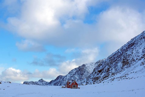 A lonely red house in the middle of a snowy winter landscape in front of majestic mountains,