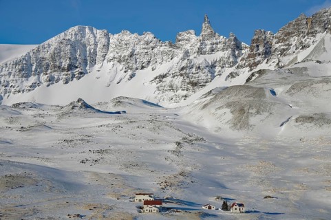 Snow-covered mountains with small houses in the foreground under a clear blue sky, winter,