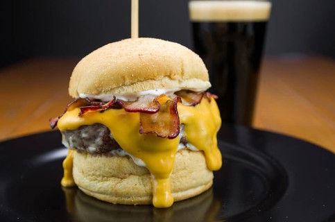 Close-up of tasty homemade bacon burger and cheddar sauce on wooden table and black background