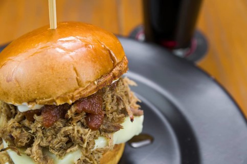 Close-up of tasty homemade pulled pork burger on wooden table and black background