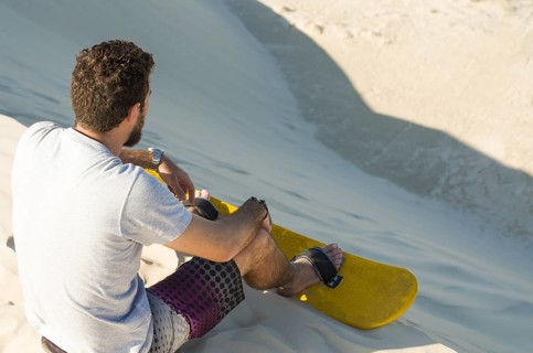 Young man on his back looking at the sand dunes, preparing to practice sandboarding