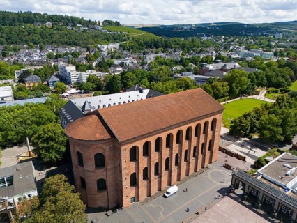 Ancient Roman building made of brick, seen from above, surrounded by city elements and green trees