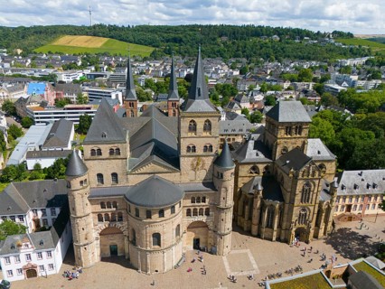 Historic cathedral with towers, surrounded by cityscape and hills under blue sky in Trier, aerial