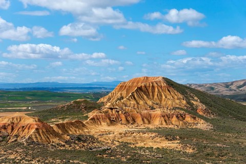 View of a large rocky hill with valley floor under a blue sky with clouds, Bardenas Reales Natural