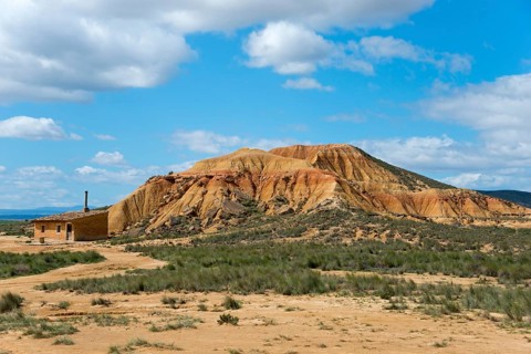 Small building in front of a rocky hill in an arid landscape under a cloudy sky, Bardenas Reales