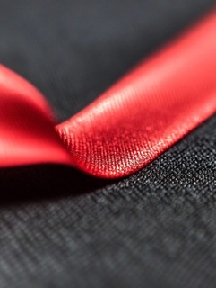 Glossy red ribbon lying on a textured black background, AI generated