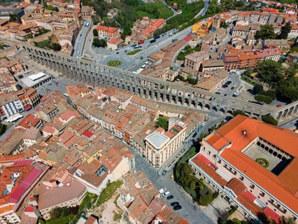 Aerial view of a city crossed by a long, historic aqueduct, surrounded by tiled roofs and street