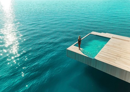 A woman stands by an infinity pool extended over the clear ocean, radiating tranquility and luxury,