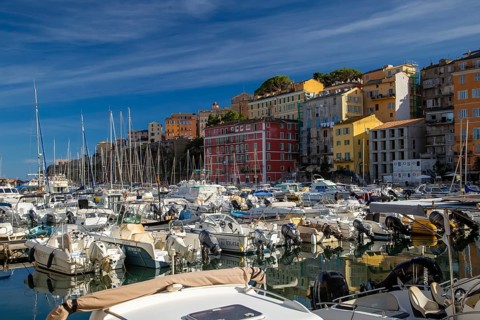 Boats at a lively marina in Corsica, surrounded by colourful buildings under a clear blue sky,
