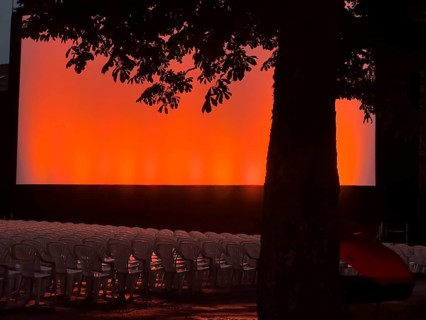 Rows of chairs and a tree in front of a red and orange illuminated screen in the open-air cinema