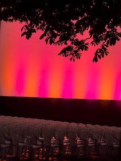 Empty rows of seats in the open-air cinema in front of a brightly lit stage, illuminated in red and