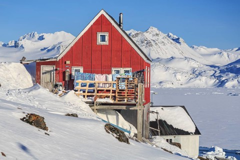 Typical Greenlandic house in front of fjord and snowy mountains, sunny, Inuit settlement, winter,