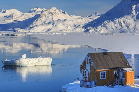Typical Greenlandic house in front of icebergs, fjord and snowy mountains, sunny, Inuit settlement,