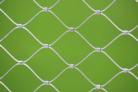 Mesh screen made of interwoven metal cables. The background is a uniform green colour. This image