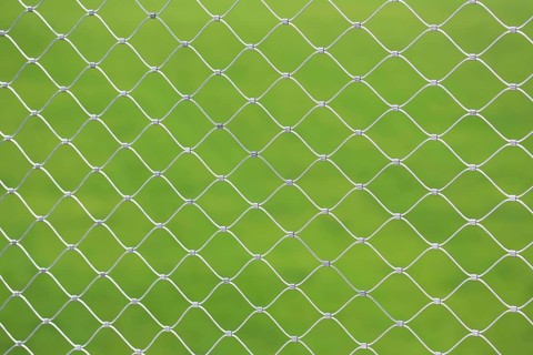 Mesh screen made of interwoven metal cables. The background is a uniform green colour. This image