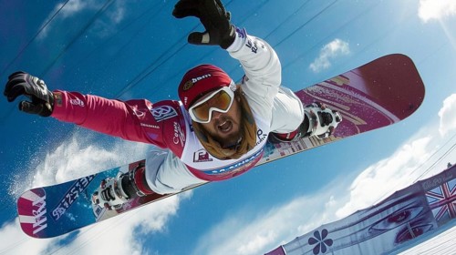 Snowboarder in mid-air, executing a jump against a bright blue sky, displaying dynamism and