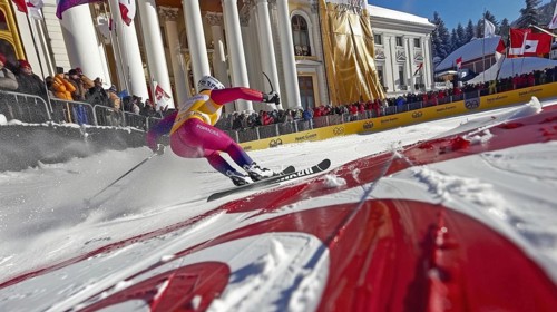 Ski racer speeding down a slope towards the finish line while a crowd watches during a winter
