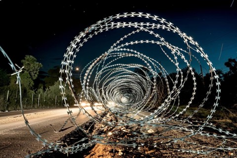 Spiral barbed wire installation alongside a road at night, creating a dramatic, secure environment,