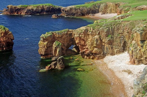 A stretch of coastline with rocky cliffs, a natural rock arch and clear blue sea water, Eshaness,