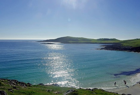 Sparkling sea with a rocky coastline, tranquil atmosphere and people on the beach, Scalloway,