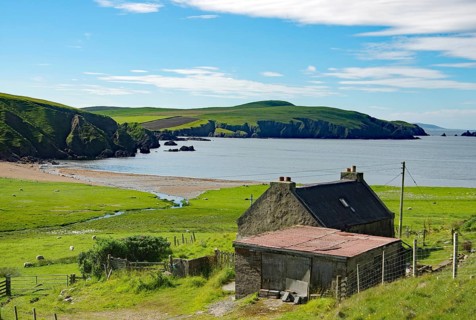 Coastal landscape with a small house near the sea, green hills and beach under a cloudy sky, crime