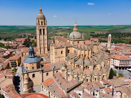 Aerial view of a historic city with a large church and red roofs under a clear blue sky, surrounded