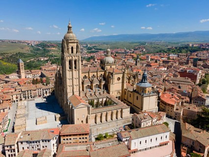Large church in a medieval town, surrounded by red roofs and historic buildings, under a blue sky
