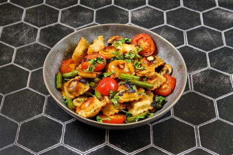 Fried ravioli with green beans, tomato and champignon mushrooms in a plate
